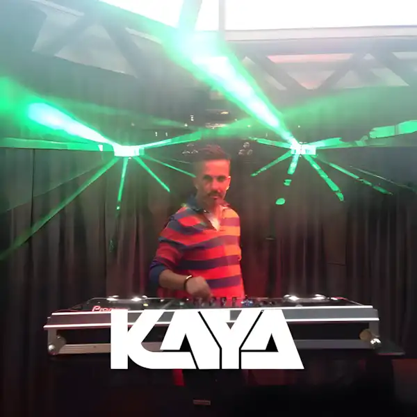 A DJ stands at a mixing console under green laser lights, creating an electric atmosphere as the word "KAYA" shines in the foreground. This scene celebrates artists who turn sound into electrifying experiences.